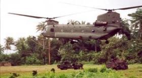 Colour photo of an RAF Chinook with a land rover underslung delivering into a jungle environment