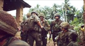 Colour photo of 6 Paras talking whilst wearing camo uniform with a jungle background