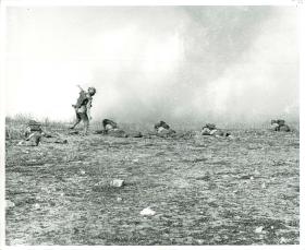 Paratrooper throws a grenade while others take cover on the ground. July, 1943.