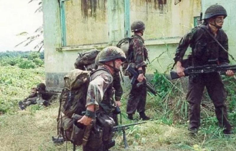 Colour photo of Paras in camo uniforms taking cover by a building