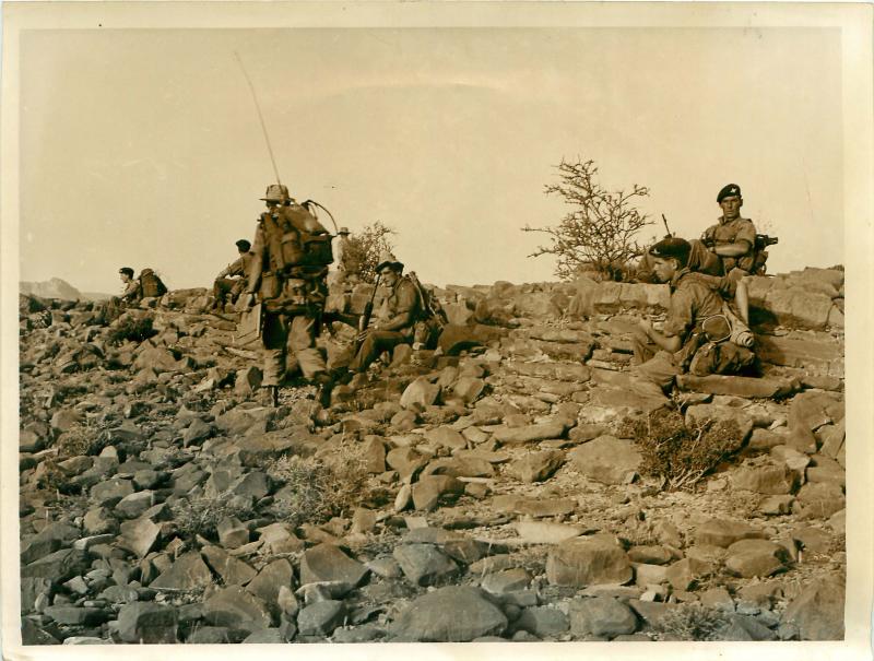 Men of 3 PARA D Company wait to move forward on rocky terrain.